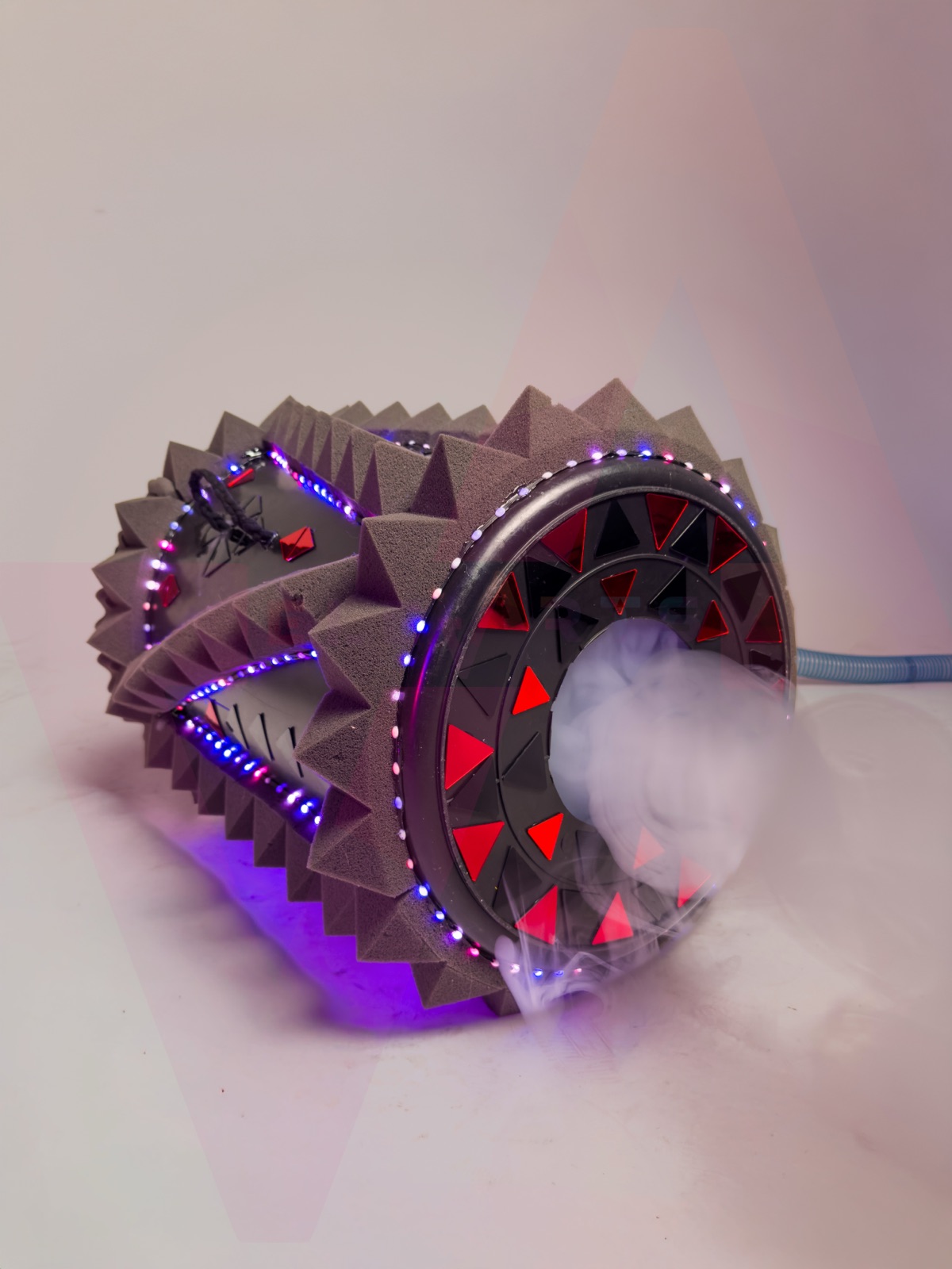 Vortex Fog Cannon lansând un inel dens de fum, cu benzi LED aprinse în albastru și roșu de-a lungul corpului din spumă